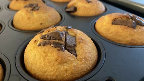 Eine Reihe goldbrauner Muffins mit Schokoladensplittern befindet sich in einer Muffinform, frisch gebacken und köstlich duftend.