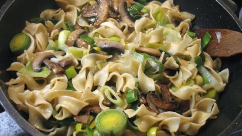 Die Bandnudeln und Pilze werden in einer Pfanne mit Lauch goldbraun gebraten, um eine schmackhafte Mahlzeit zu kreieren.
