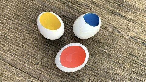 Drei bemalte Ostereier mit bunten Innenflächen liegen auf einem rustikalen Holztisch.