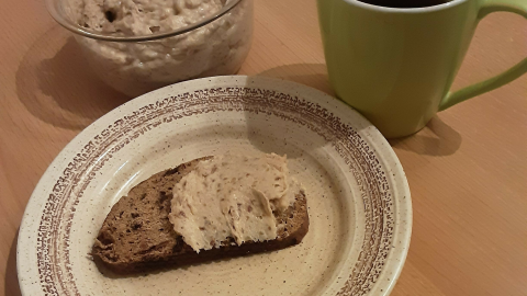 Eine Scheibe Vollkornbrot liegt auf einem Teller, bestrichen mit einem frischen Brotaufstrich, neben einer Tasse Kaffee.