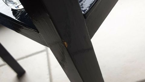 Ein schwarzes Möbelstück hat an einer Ecke einen Lackkratzer, während es auf einem hellen Fliesenboden steht.