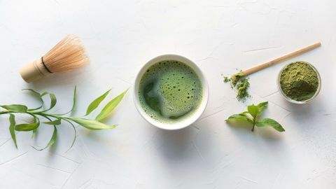 Eine Schüssel mit schaumigem Matcha wird mit einem kleinen Besen bearbeitet, um das grüne Getränk zuzubereiten.