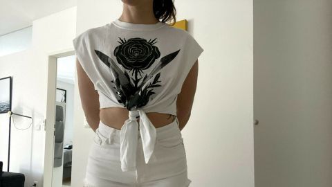 Ein umfunktioniertes T-Shirt, als Crop Top gebunden, wird von einer Person in einer hellen Umgebung getragen.
