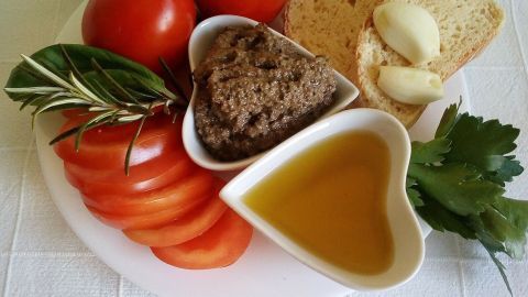Ein herzförmiger Teller enthält Tapenade, frische Tomaten, Brot, Olivenöl und Kräuter zur Zubereitung.