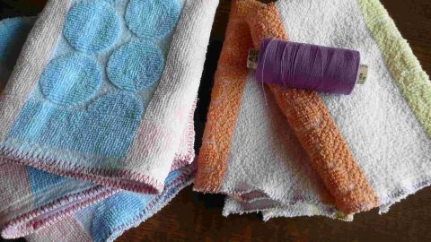 Bunte Frottee-Handtücher liegen auf einem Tisch, während eine lila Nähgarnrolle daneben darauf wartet, verwendet zu werden.