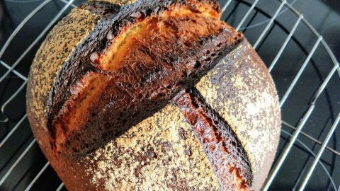 Ein frisch gebackenes Dinkel-Sauerteigbrot liegt auf einem Kuchengitter, während es abkühlt und seine knusprige Kruste zeigt.
