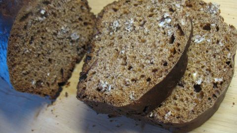 Drei Scheiben dunkles Brot liegen auf einem Holzbrett, bereit zum Servieren als Bananen-Joghurt-Frühstücksbrot.