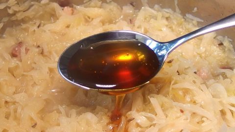 Ein Löffel mit dunkler Flüssigkeit ist in mildem Sauerkraut eingetaucht, das in einem Topf zubereitet wird.