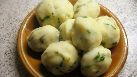 Zarte Kartoffel-Bärlauch-Knödel liegen in einer braunen Schale auf einer hellen, strukturierten Oberfläche.