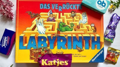 Ein farbenfrohes Gesellschaftsspiel "Das verrückte Labyrinth" liegt im Mittelpunkt, umgeben von Süßigkeiten und Pflegeprodukten.