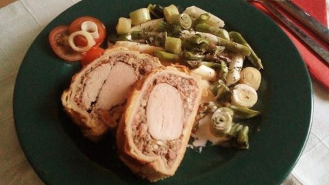 Ein saftiges Schweinefilet Wellington liegt auf einem grünen Teller, umgeben von frischem Spargel und Tomaten.