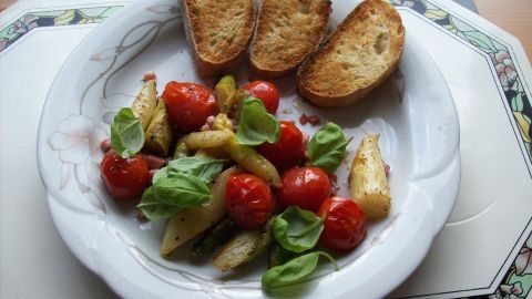 Bunte Spargelpfanne mit Tomaten, frischem Basilikum und knusprigem Brot auf einem weißen Teller.