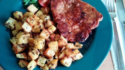 Goldene Ofenkartoffeln werden mit einem saftigen Stück Fleisch auf einem grünen Teller serviert, garniert mit Tomaten.