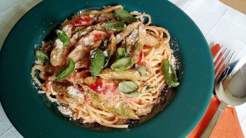 Eine große Portion Spaghetti mit Spargel und Tomaten wird auf einem grünen Teller serviert, umgeben von Besteck und Servietten.