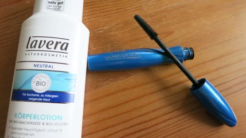 Eine Wimperntusche liegt geöffnet auf einem Holztisch neben einem Shampoo. Die Verpackungen sind klar und gut sichtbar.