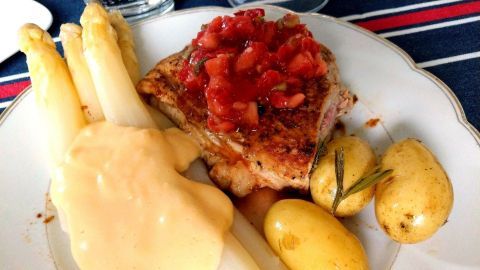 Ein gefülltes Schnitzel mit Tomatensauce liegt auf einem Teller, umgeben von Spargel und kleinen Kartoffeln.