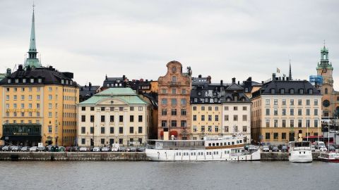 Eine weiße Yacht liegt am Ufer, während historische Gebäude mit grünen Dächern die Wasserfront in einer Stadt prägen.