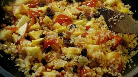 Eine bunte Pfanne mit Bulgur, Tomaten und Schinken wird gerührt, um die Zutaten gut zu vermischen.