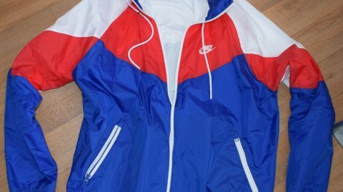 Eine bunte Nike-Jacke liegt flach auf einem Holzfußboden, bereit zum Spenden oder für die Entsorgung von Altkleidern.