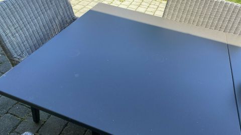 Ein Metallgartentisch steht sauber und fast wie neu in einem gepflegten Garten, umgeben von modernen Stühlen.