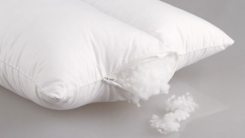 Ein Kopfkissen mit Reißverschluss, aus dem fluffige Füllung herausquillt, auf einem grauen Untergrund.