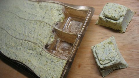 Würzige Bärlauch-Butter in einer Form, einige Stücke sind herausgenommen und liegen auf einem Holzbrett.