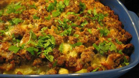 Ein frisch gebackenes Kartoffel-Karotten-Gratin mit Hack, bedeckt mit grünen Kräutern, erscheint appetitlich in einer blauen Auflaufform.