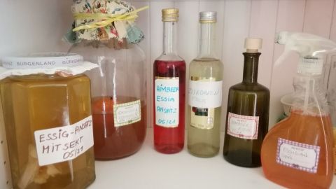 Ein Glas mit Essigansatz steht auf einem Regal, umgeben von verschiedenen Flaschen, die Essigsorten enthalten.