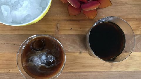 Ein Glas vietnamesischer Kaffee mit Eiswürfeln neben einer Schüssel mit crushed ice und einer dekorativen Blume auf Holz.