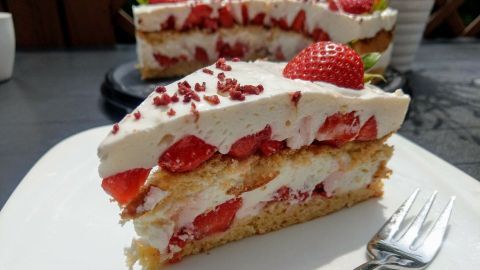 Eine saftige Erdbeertorte mit Frischkäse ruht auf einem weißen Teller, während ein Stück davon bereits herausgeschnitten ist.