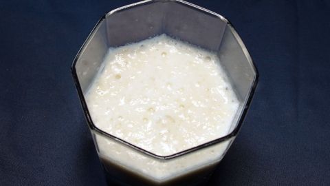 Ein cremiger Bananenshake steht in einem viereckigen Glas auf einem dunklen Tisch, bereit zum Genießen.