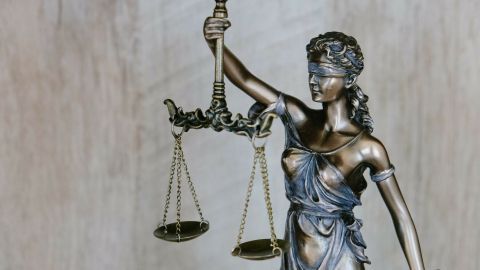 Eine Statue der Justitia hält in einer Hand eine Waage, symbolisch für Gerechtigkeit, vor einem neutralen Hintergrund.