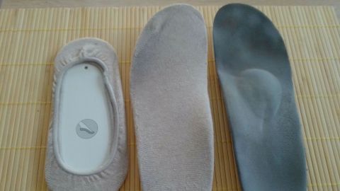 Drei Schuheinlagen liegen auf einem Bambusuntergrund, während Füßlinge ordentlich zum Bespannen vorbereitet werden.