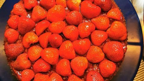 Der Schokoladenboden ist mit glänzenden Erdbeeren bedeckt und auf einem blauen Teller platziert, umgeben von einer Metalloberfläche.