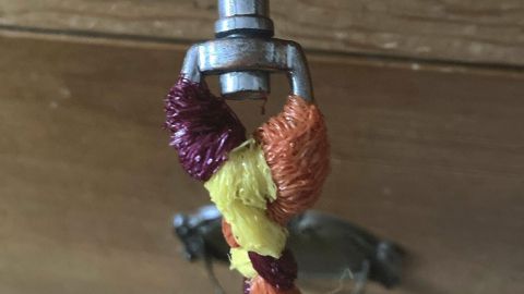 Eine bunte Hundeleine hängt an einem metallischen Karabiner, vor einer hölzernen Wand, bereit zur Verwendung.