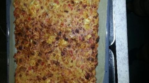 Eine krosse Schüttelpizza ohne Boden liegt auf einem Backblech, frisch gebacken mit einer goldbraunen Oberfläche.