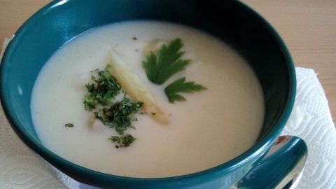 Eine schlichte Schüssel mit sahniger Spargelcremesuppe, garniert mit frischen Kräutern, steht auf einem weißen Teller.