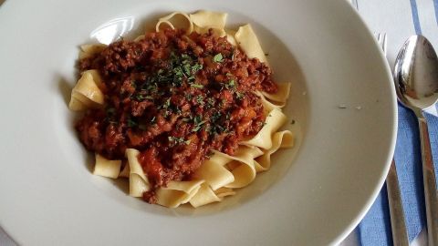 Eine Schüssel mit Tagliatelle ist mit reichhaltigem Ragù Bolognese bedeckt und liegt auf einem rot-weiß gestreiften Tischläufer.