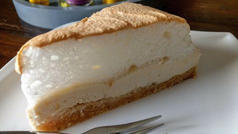 Ein Stück Topfenschnitte liegt appetitlich auf einem weißen Teller, während eine Gabel daneben bereit zum Essen ist.