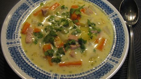 Eine cremige Karotten-Kohlrabi-Suppe wird in einer dekorativen Schüssel serviert, garniert mit frischem Gemüse und Kräutern.