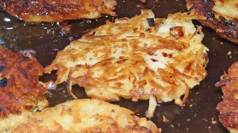 Knusprige Kartoffelpuffer braten in einer Pfanne, umgeben von weiteren goldbraunen, köstlichen Kartoffelscheiben.
