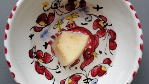 Ein bunter Teller zeigt ein Stück Obst, das als Hinweis zum Fang von Fruchtfliegen dient, auf einer grauen Oberfläche.