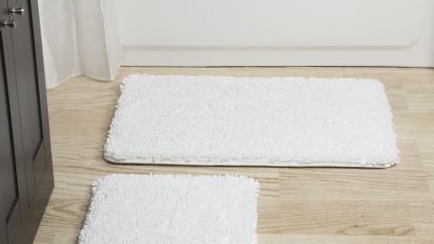 Weißer Badteppich liegt auf einem hellen Holzboden vor einer Badewanne, bereit zur Reparatur statt zur Entsorgung.