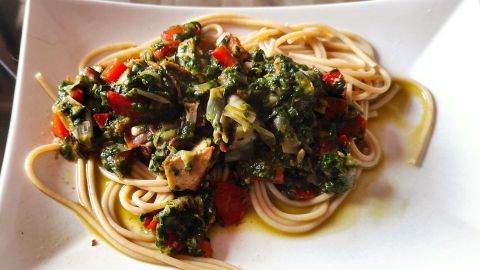 Dünne Spaghetti liegen auf einem Teller, garniert mit buntem Gemüse und Feta, umgeben von grünem Olivenöl.