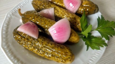 Eingelegte Gurken liegen auf einem weißen Teller, dekoriert mit roten Zwiebeln und Petersilie, appetitlich serviert.