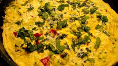 Ein buntes Gemüse-Omelett mit Zucchini und Paprika liegt in einer Pfanne und ist mit frischem Kräutern garniert.