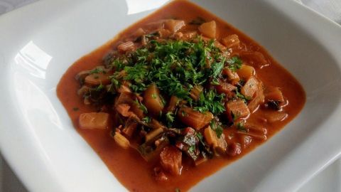 Ein Teller mit würziger Mangoldsuppe zeigt eine dicke, tomatige Brühe, garniert mit frischem, grünen Kräutern, umgeben von Gläsern.