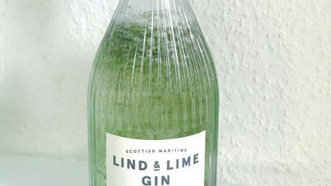 Eine grüne Gin-Flasche steht auf einer glatten Oberfläche, während sie für das Mixen von Salatkräutern bereit ist.