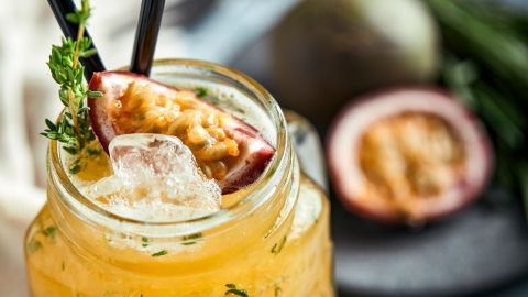 Ein Glas mit Maracujaschnaps enthält Eis und ist mit Kräutern dekoriert, daneben eine halbierte Passionsfrucht.