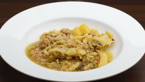 Ein dampfender Teller mit Schmorkohl und Hackfleisch liegt auf einem Holzuntergrund. Herzhaft und rustikal angerichtet.